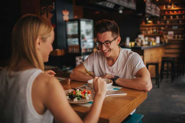 Eine Nahaufnahme eines jungen Paares bei einem romantischen Date in einem Restaurant, das gemeinsam am Tisch sitzt, isst und lacht.